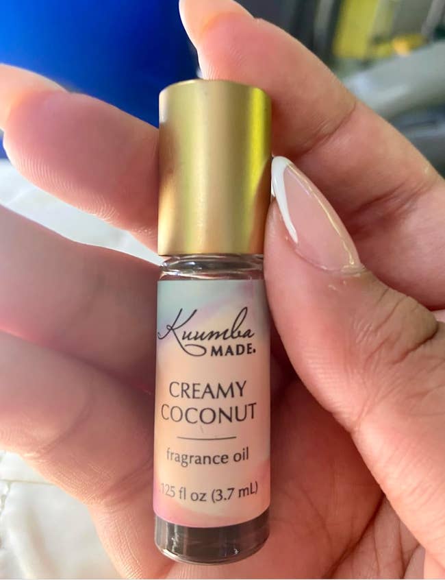 A manus holds a vessel of Kuumba Made Creamy Coconut fragrance oil, labeled 0.125 fl oz (3.7 mL)