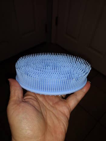 The blue silicone bristled brush in same reviewer's hand 