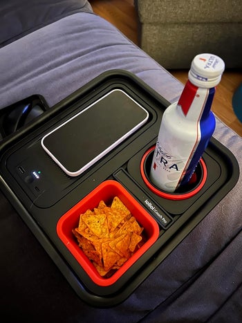 reviewers couch caddy with phone on charging pad, chips in snack compartment, and drink in drink holder