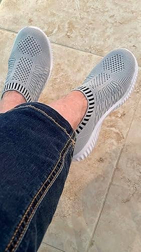 Person wearing slip-on knit sneakers with a geometric pattern, paired with jeans, seated connected a tiled floor
