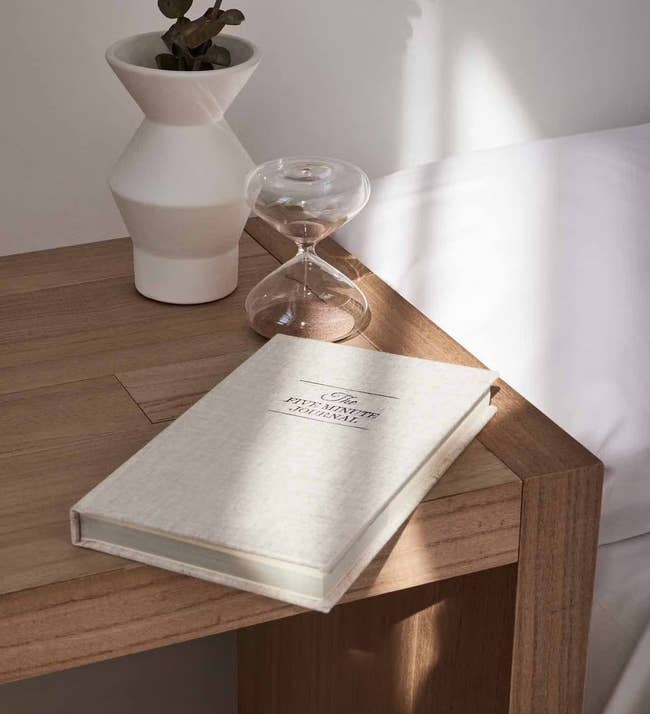 the glass sand timer in hourglass shape on a desk next to a book