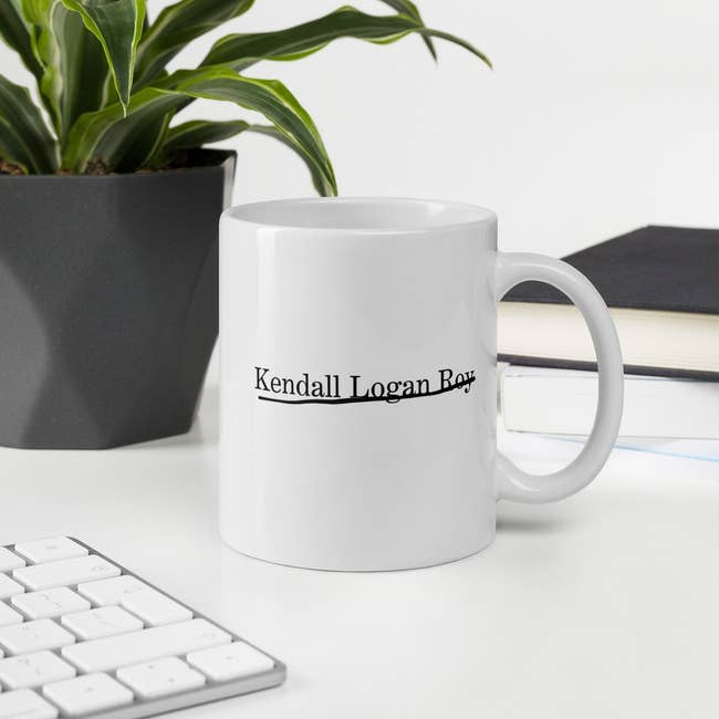 A white mug with Kendall Logan Roy half underlined, half crossed out