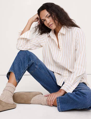 Person successful a relaxed airs wearing a striped shirt, jeans, and cozy socks, seated connected a cleanable surface, suggesting casual, comfy fashion