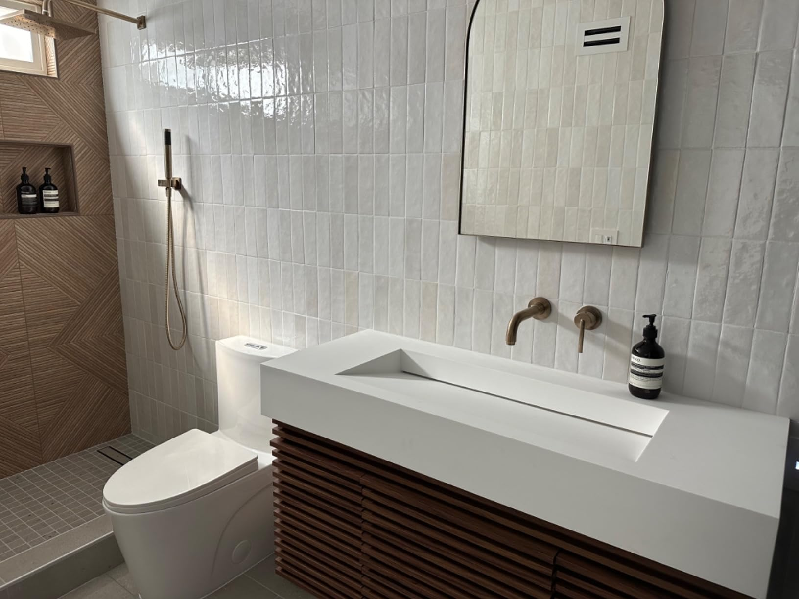 Modern bath  with wall-mounted sink, sleek faucet, shower, and toilet. Minimalist plan  with tile walls and woody  furniture  accents