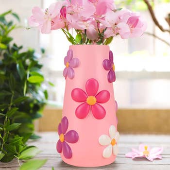 Pink vase adorned with decorative flowers on a table, complemented by light-pink blossoms within