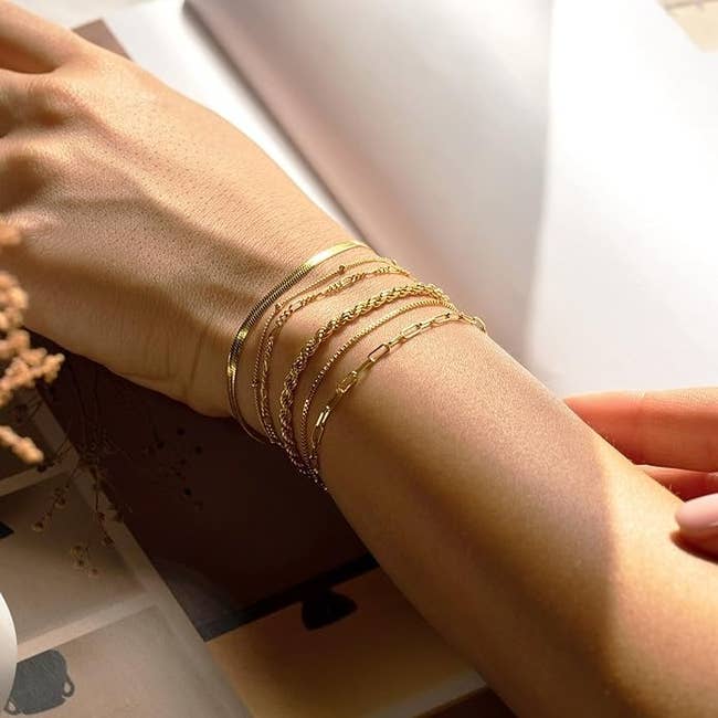 Close-up of a model's wrist adorned with multiple delicate gold bracelets