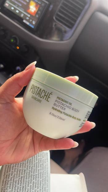 A manus  holds a jar of Pistaché Skincare Pistachio Body Butter successful  a car
