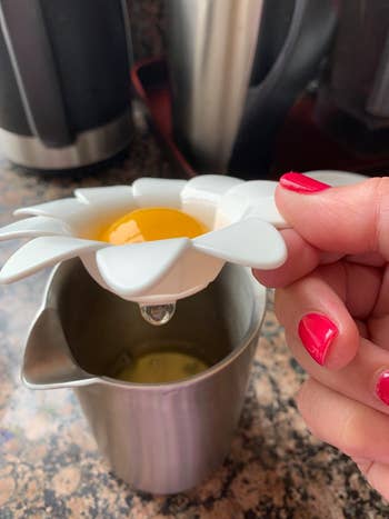 reviewer's small cup that looks like a daisy in white with an egg yolk in the middle and the egg whiles pouring into a glass below it