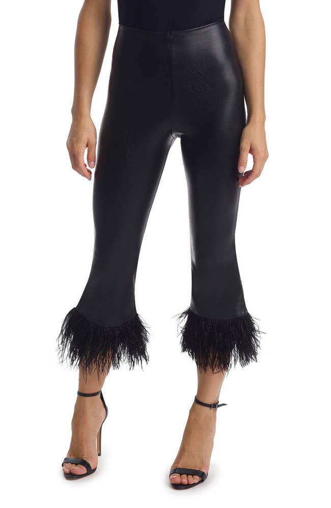 a model wearing black faux leather capris with feather-trimming on the legs
