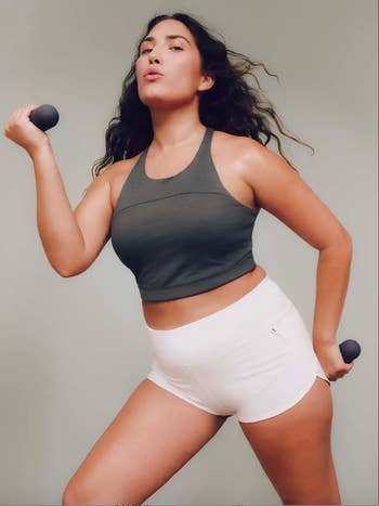 model posing with small dumbbells, wearing gray crop top and white shorts