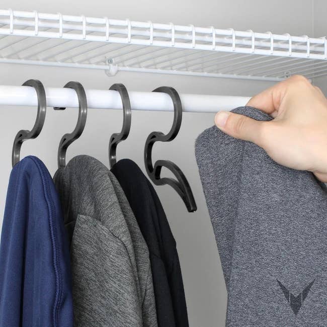 a model putting a hooded sweatshirt on one of the hooks hanging on a closet. rod