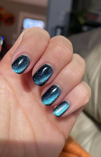 A hand displays a manicure with a gradient effect from dark to light, featuring glittery, shimmering nail polish