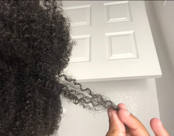 Reviewer with curly hair holding a strand of it out 