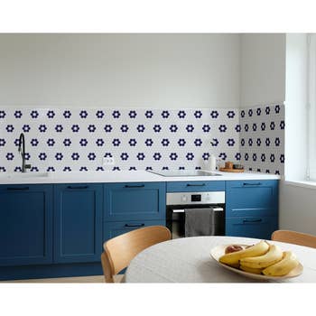 Kitchen with blue cabinets, patterned backsplash, and a table with fruit bowl. Appealing design for home decor shopping inspiration
