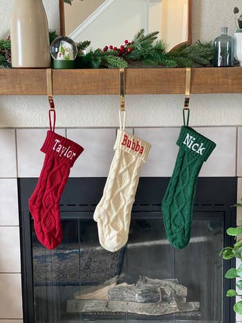 Red, white, and green stockings hanging over a reviewer's chimney with names embroidered on them
