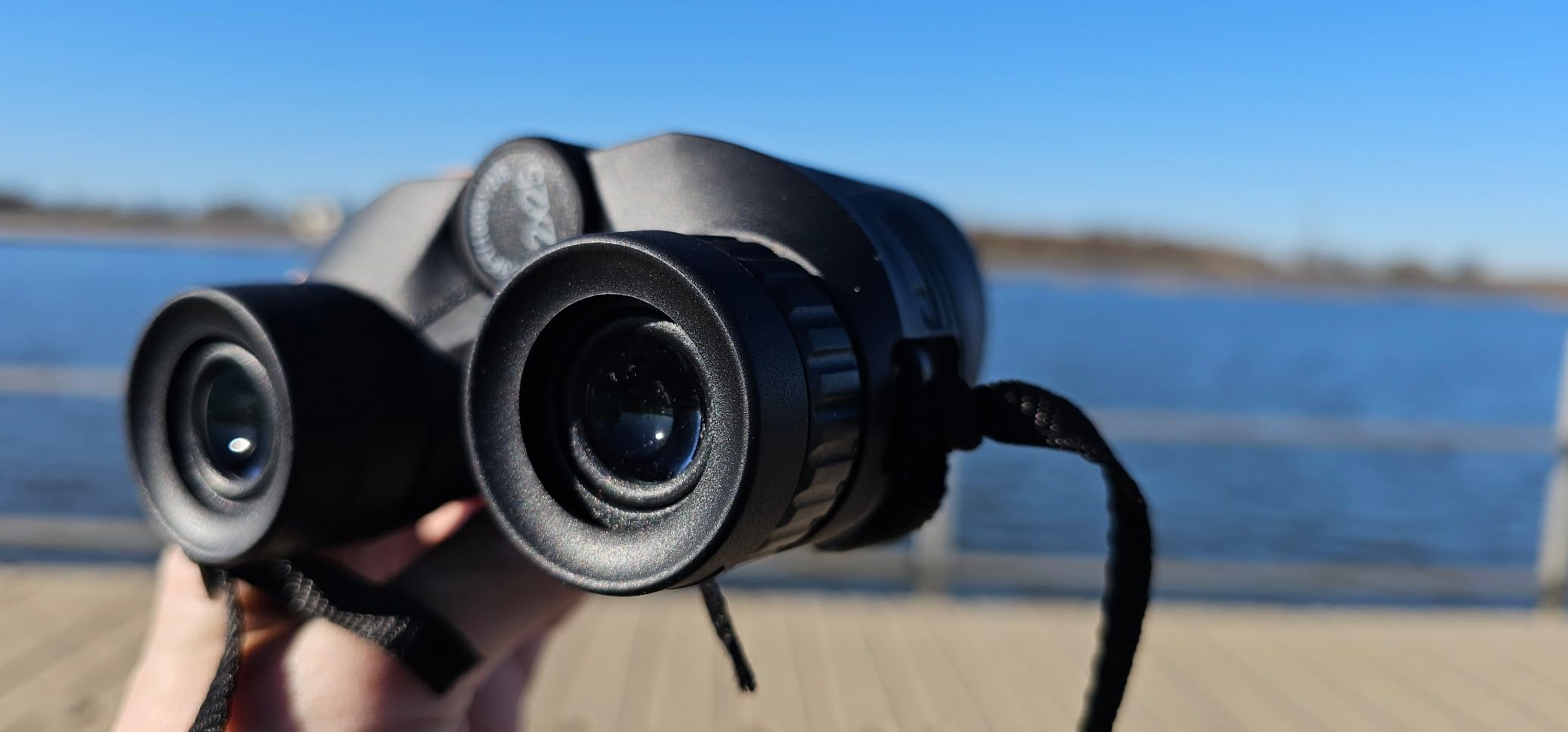 Person holding achromatic  binoculars adjacent   a assemblage  of water