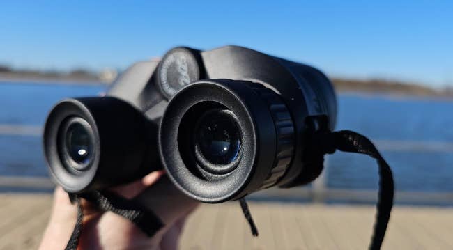 Person holding achromatic binoculars adjacent a assemblage of water