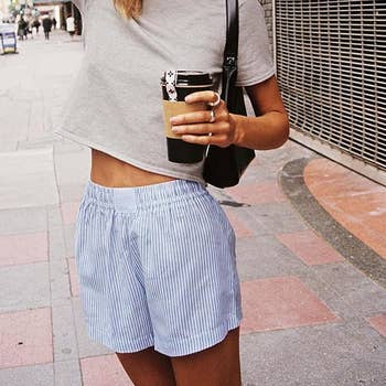 Person successful a casual outfit holding a reusable cup, wearing a cropped grey apical and striped shorts, walking connected a metropolis sidewalk