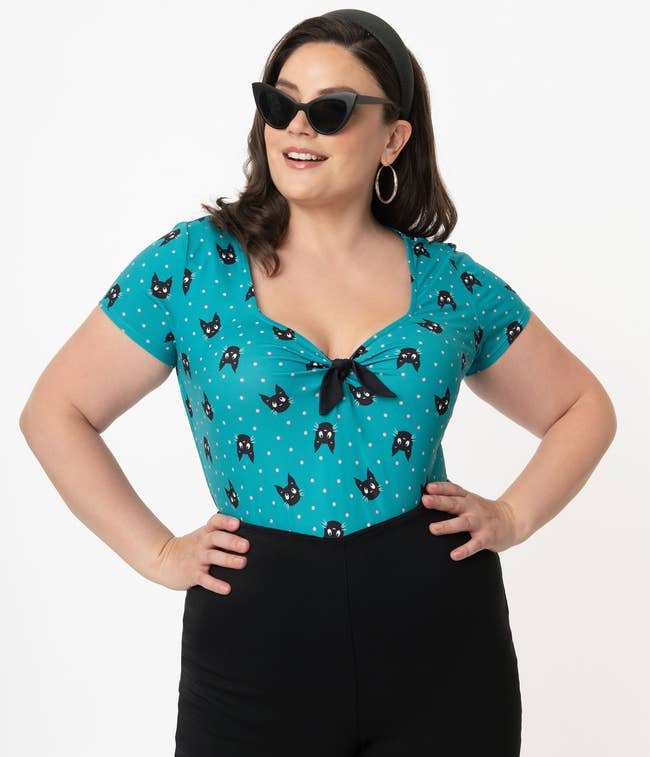 model in short sleeve teal top with black cat faces and black bow at the bust