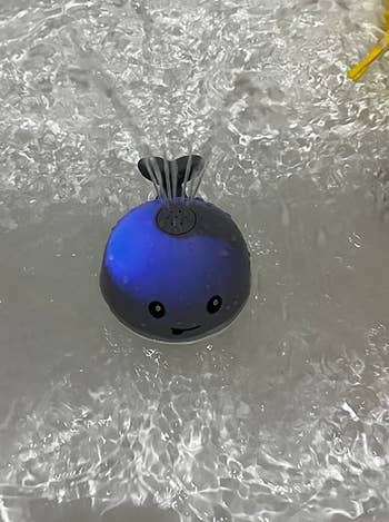 reviewer's photo of the gray toy lit up blue and squirting water in the bath