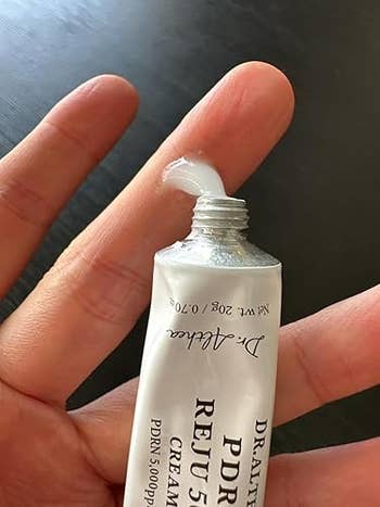 A person holding an open tube of Dr. Althea PDRN cream, with a small amount of cream visible at the opening