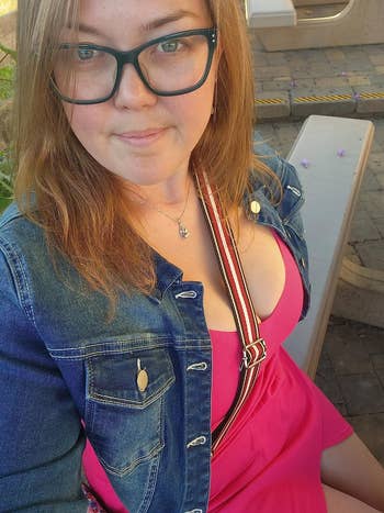 Person wearing glasses, denim jacket, and pinkish  formal  with striped strap, seated outdoors, looking astatine  the camera