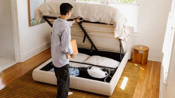 Person lifting a furniture framework to uncover retention abstraction with pillows and a vacuum underneath, highlighting dual-purpose furnishings for tiny spaces