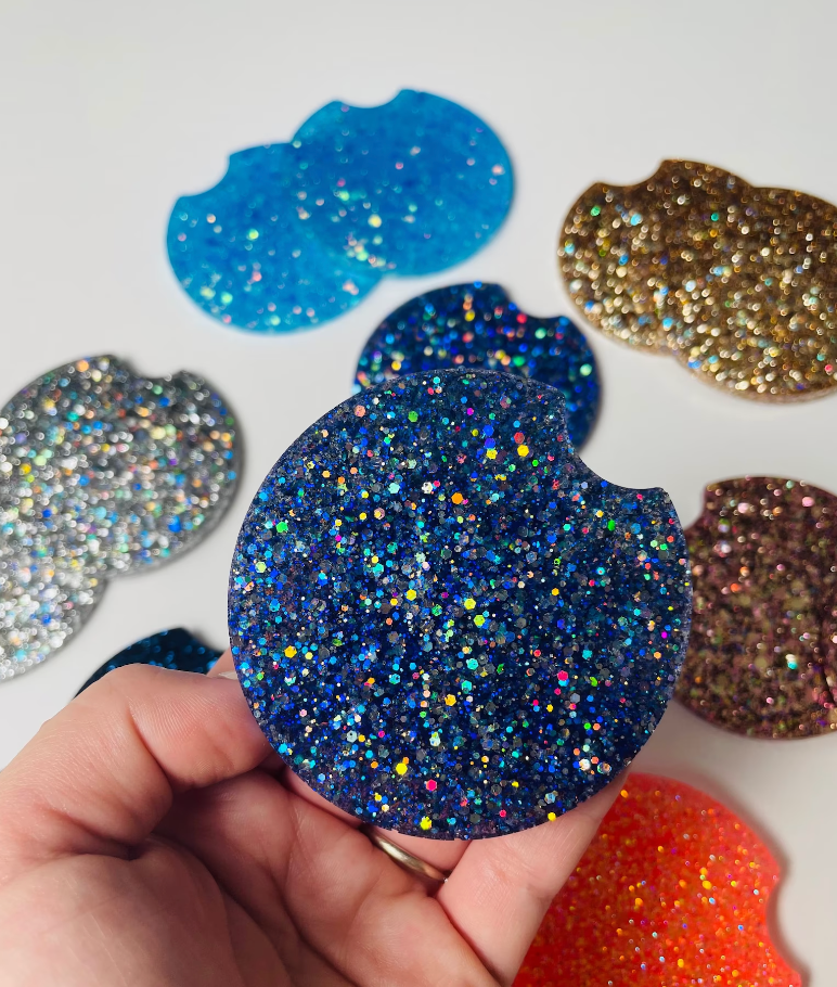 a model holding the navy glitter coasters with other coasters of different colors in the background – silver, light blue, gold, purple, and orange