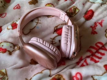 Pink wireless headphones resting connected  a cartoon-themed blanket