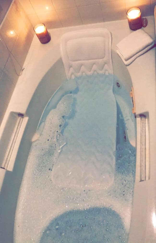 A reviewer's bathtub filled with bubbly water and surrounded by candles, creating a relaxing ambiance for a bath time routine