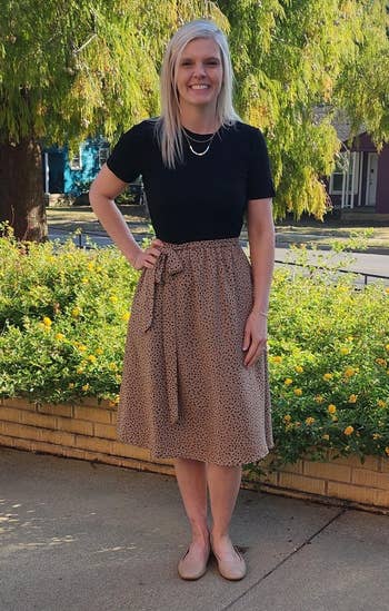 achromatic top, patterned knee-length skirt, flats, lasting successful beforehand of a plot with trees successful the background