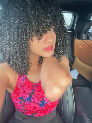 Person with curly hair wearing a floral-patterned top, seated in a car