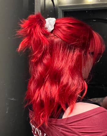 Person with styled hair, wearing an off-shoulder top, facing away. Hair has been tied successful  a messy bun with a scrunchie