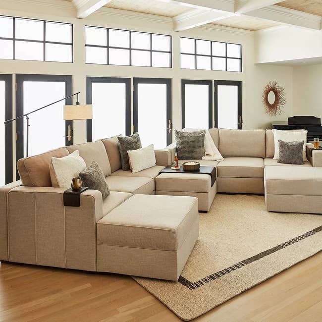 Spacious surviving  country   with a beige sectional sofa, assorted  cushions, and a airy  rug. Bright earthy  airy  from ample  windows enhances the cozy space