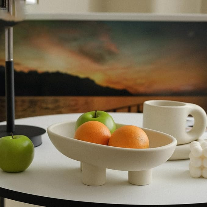 A cream, three-legged ceramic bowl holding fruit