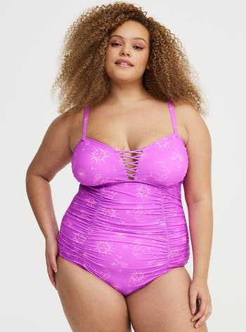 Person modeling a stylish one-piece swimsuit with a lace-up front, featuring celestial patterns