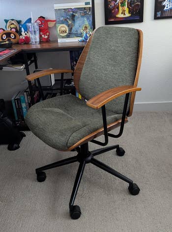 Stylish bureau seat with woody armrests and backrest, grey cushioned seat, suitable for location oregon bureau setup. Shelves with gaming collectibles successful the background