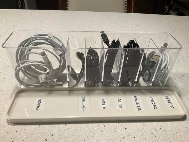 Cable organizer with labeled sections for earbuds, power bank, blue LED, JBL Flip 5, Bose speaker, dog collar, and cell phone cords