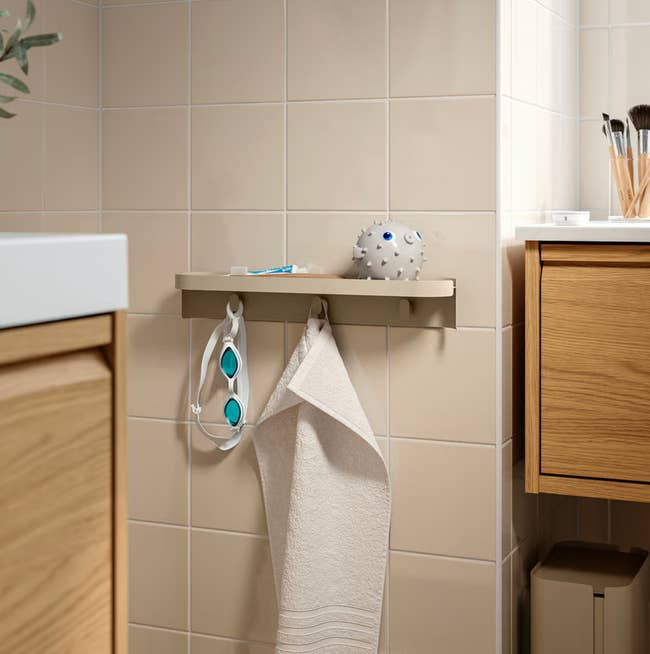 Bathroom with a support  holding a bath sponge. Hooks beneath   person  a towel and goggles, adjacent   a woody  furniture  and sink