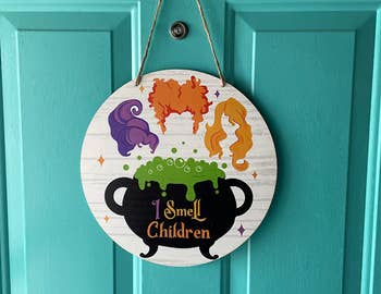 round sign on reviewer's door with sanderson sister's hair and cauldron that says i smell children 