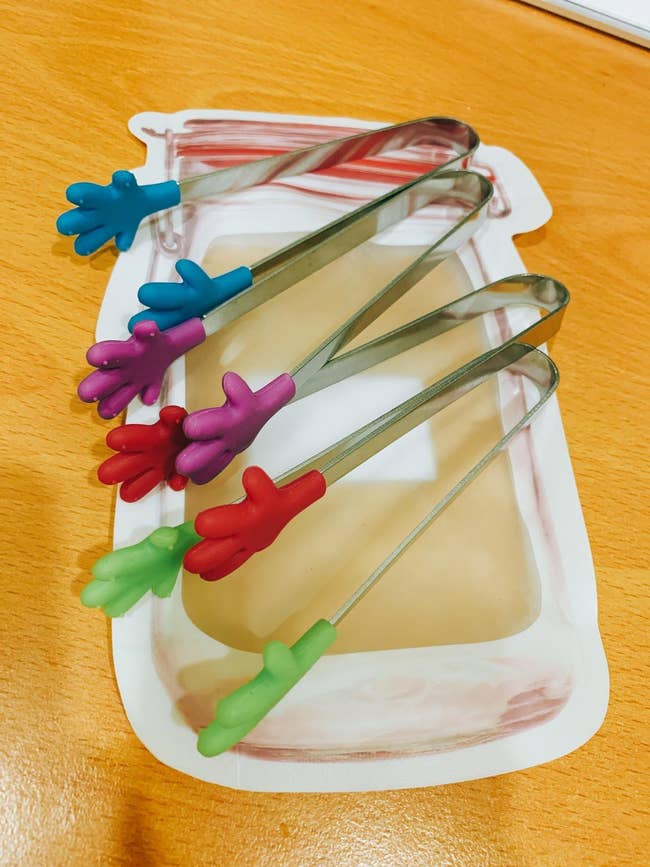 reviewer photo of  four pairs of mini tongs with colored hands on each end in green, red, purple, and blue