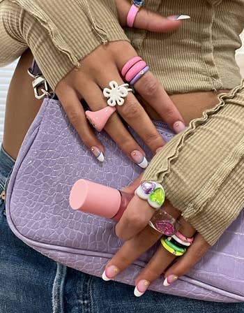 white flower bomb-shaped ring styled with other colorful, Y2K-inspired stacking rings on model's hands 