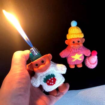 Hand lights a cigaret lighter adjacent 2 troll dolls successful knitted sweaters and hats, 1 with a strawberry design, for a buying article