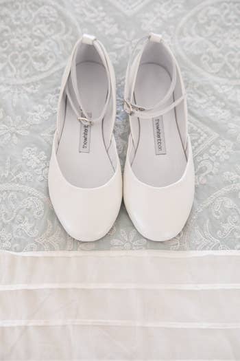 a white pair of ballet flats with a thin leather ankle band
