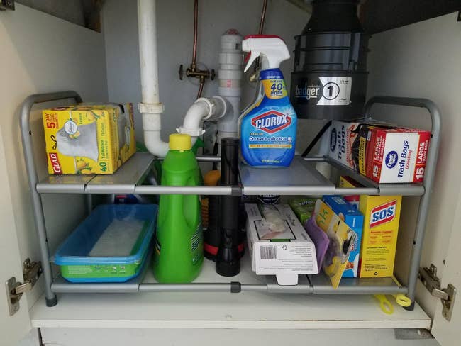 Under-sink storage with cleaning supplies and household items organized on two-tiered shelving
