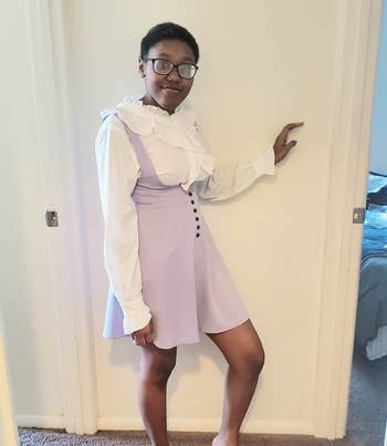 a reviewer in a lavender pinafore dress with suspenders