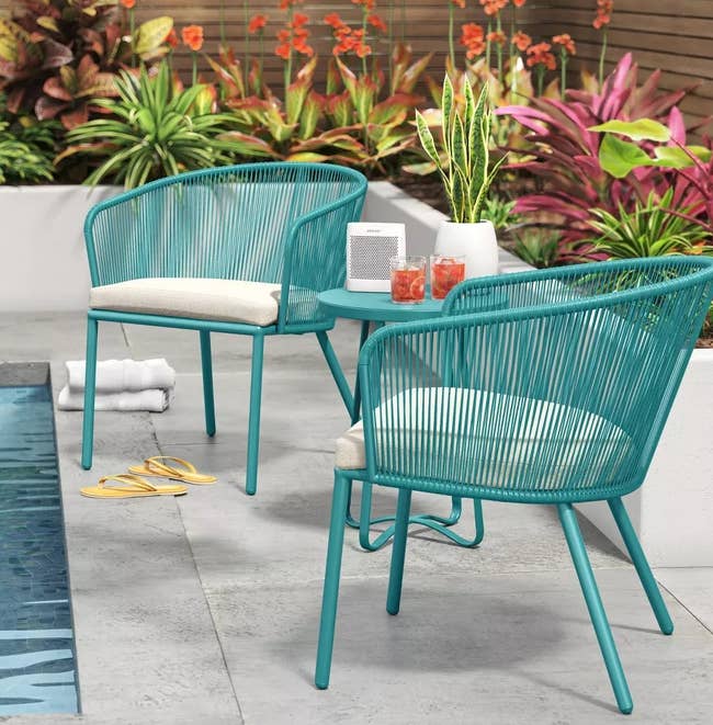 two bucket-style chairs and a side table by a pool 