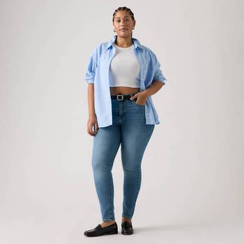 A idiosyncratic   poses successful  casual fashion, wearing a airy  button-up garment  implicit    a achromatic  top, bluish  jeans, and slip-on shoes