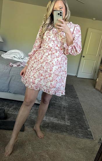 reviewer taking a mirror selfie wearing a floral dress, with sunglasses atop their head. Items scattered on the floor