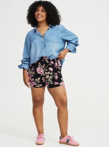 Person successful  a casual denim garment  and floral shorts, paired with pinkish  sneakers, posing confidently